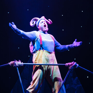 A man dressed in a goat costume with his arms open and mouth wide open.