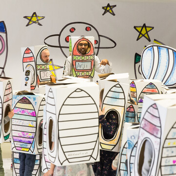 A group of people wearing paper boxes with rockets drwan on them.