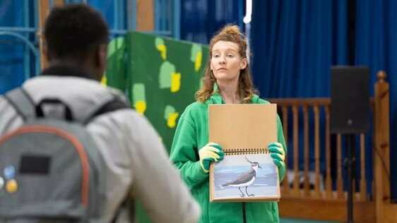 Female actor in play holding painting of a bird