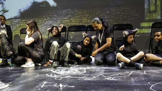 Workshop leader and school children sat around chalk drawings on the floor